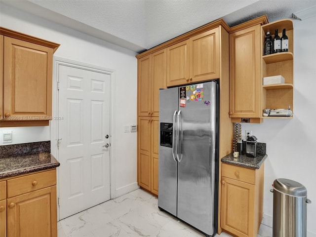 kitchen with stainless steel fridge with ice dispenser, a textured ceiling, and dark stone counters