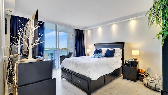 bedroom with a water view, light wood-type flooring, a wall of windows, and access to outside