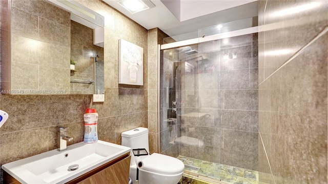 bathroom with vanity, toilet, a shower with door, and tile walls