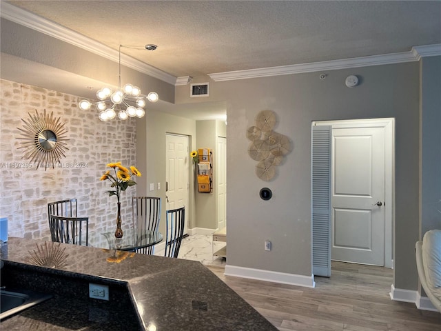 kitchen with ornamental molding, a textured ceiling, hardwood / wood-style flooring, a notable chandelier, and dark stone countertops