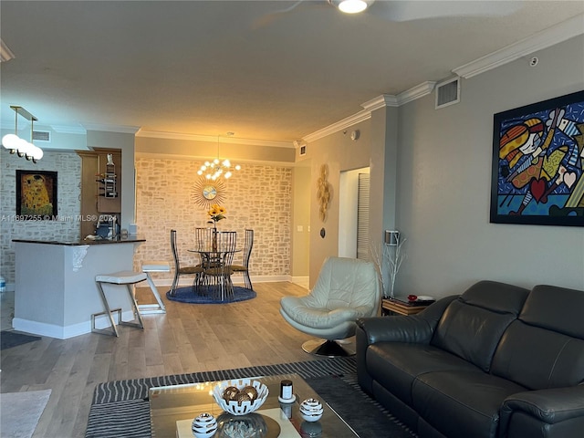 living room with hardwood / wood-style flooring, a notable chandelier, crown molding, and brick wall