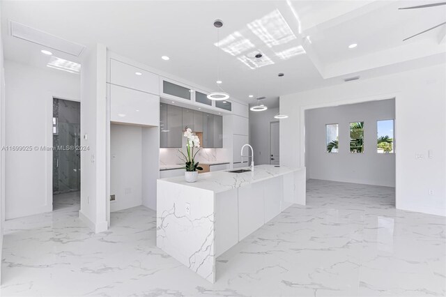 kitchen featuring light stone countertops, a kitchen island with sink, sink, pendant lighting, and white cabinets