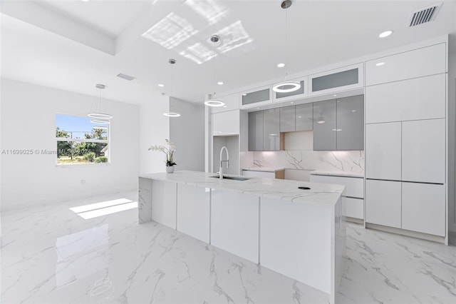 kitchen featuring pendant lighting, gray cabinetry, sink, decorative backsplash, and light stone countertops