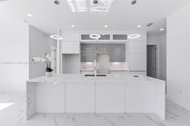 kitchen with gray cabinetry, sink, pendant lighting, and a center island with sink