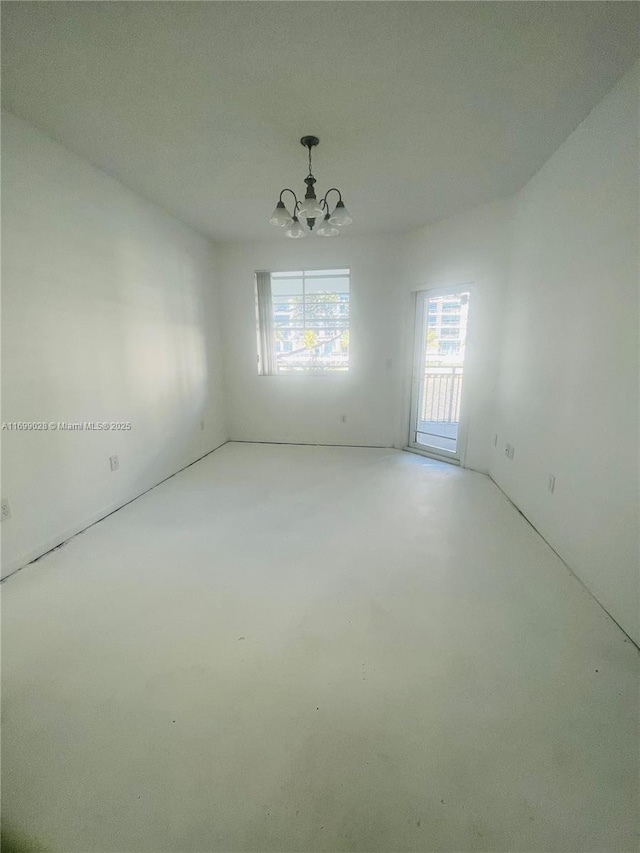 empty room with concrete flooring, a wealth of natural light, and a notable chandelier