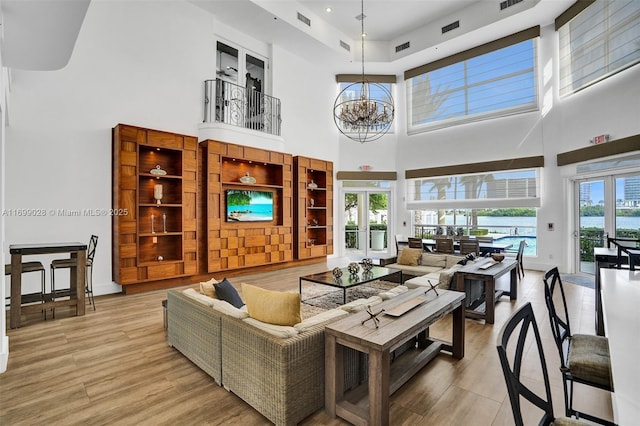 living room with plenty of natural light, an inviting chandelier, light hardwood / wood-style floors, and french doors