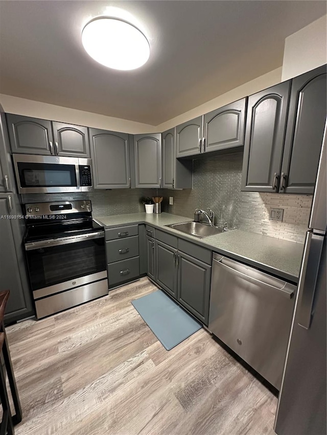 kitchen featuring decorative backsplash, appliances with stainless steel finishes, light hardwood / wood-style floors, and sink