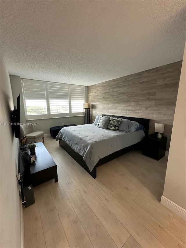 bedroom with a textured ceiling, light hardwood / wood-style flooring, and wooden walls