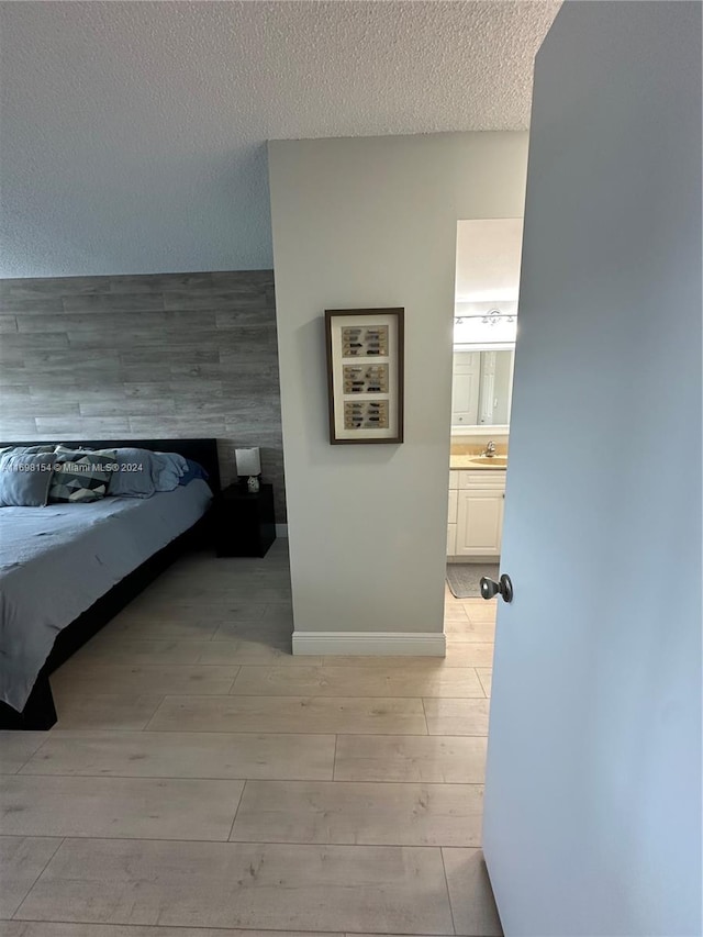 unfurnished bedroom with sink, a textured ceiling, connected bathroom, and light hardwood / wood-style flooring