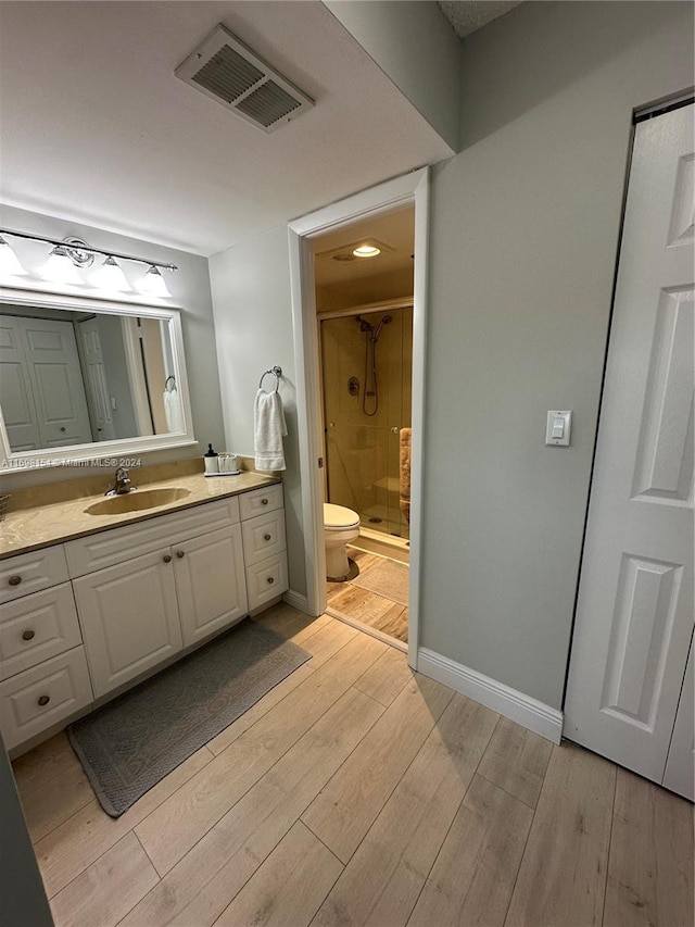 bathroom with hardwood / wood-style floors, vanity, a shower with door, and toilet