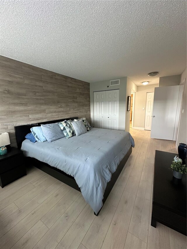 bedroom featuring a textured ceiling, light wood-type flooring, a closet, and wood walls