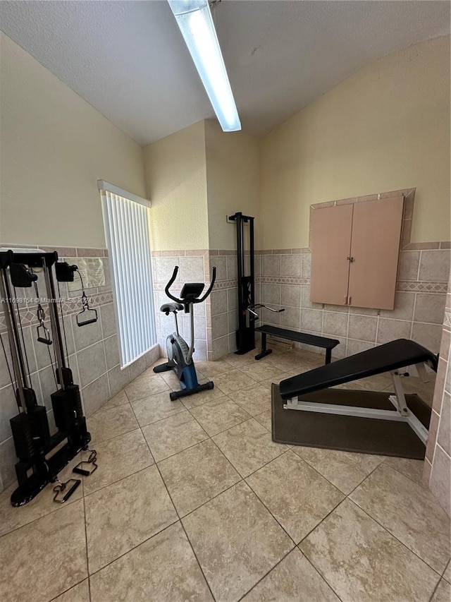 workout room with light tile patterned flooring, lofted ceiling, and tile walls