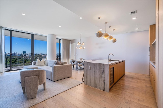 living room featuring a wall of windows, sink, a notable chandelier, and light wood-type flooring