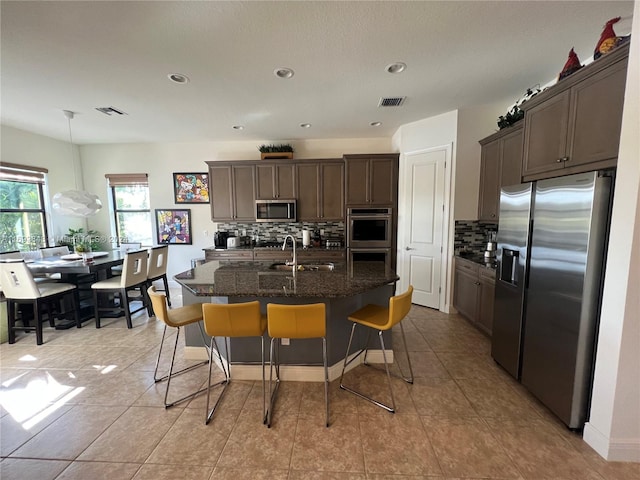 kitchen with sink, stainless steel appliances, tasteful backsplash, and an island with sink