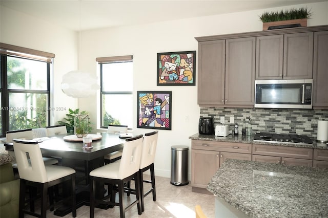 kitchen with decorative backsplash, gas stovetop, light stone countertops, and light tile patterned floors