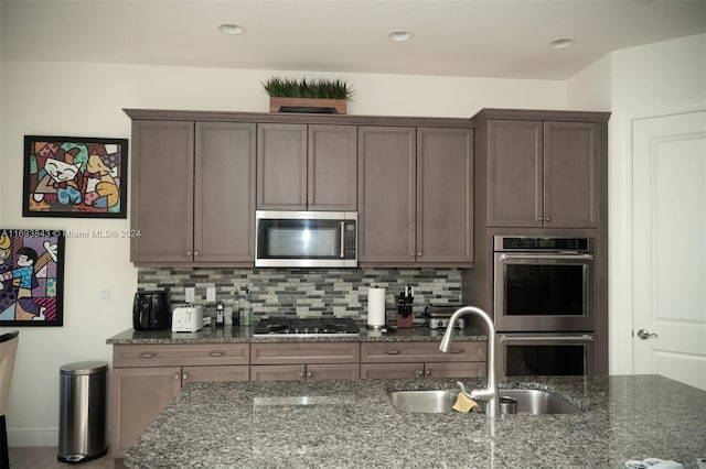 kitchen featuring decorative backsplash, appliances with stainless steel finishes, dark stone counters, and sink