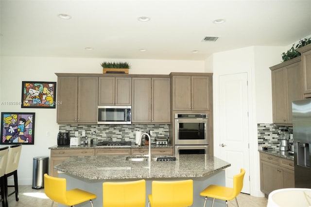 kitchen featuring appliances with stainless steel finishes, a kitchen breakfast bar, sink, stone countertops, and a center island with sink