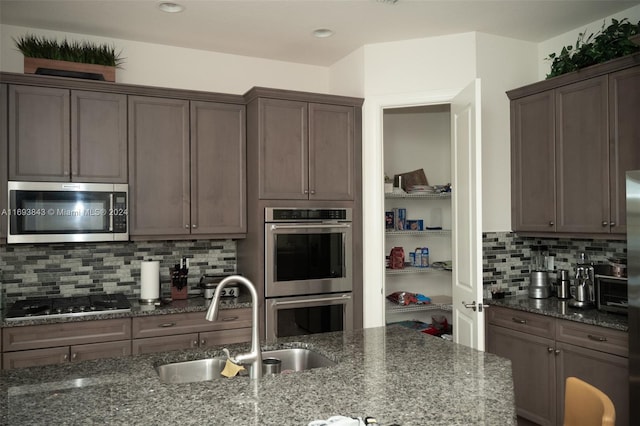 kitchen with tasteful backsplash, dark stone countertops, sink, and stainless steel appliances