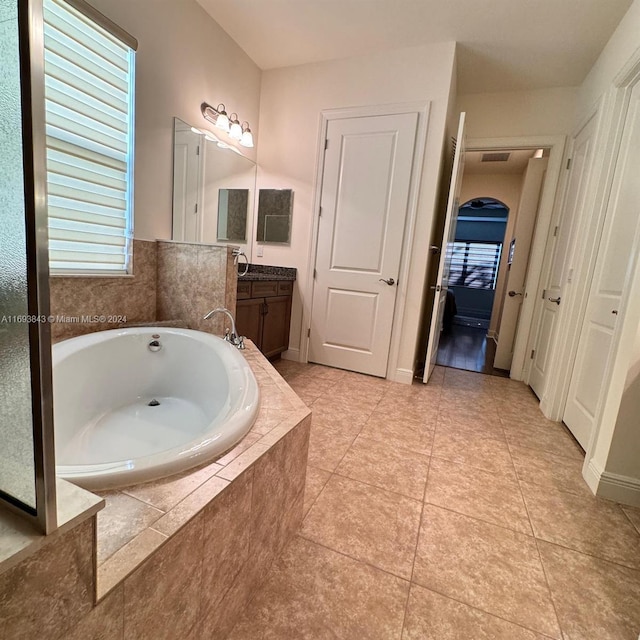 bathroom with tile patterned floors, vanity, and a relaxing tiled tub