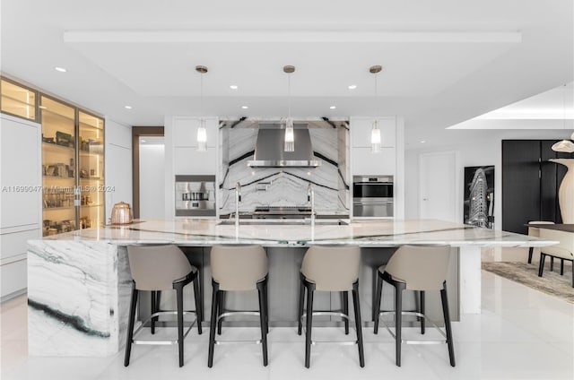 kitchen with white cabinets, a spacious island, wall chimney range hood, decorative light fixtures, and a breakfast bar area