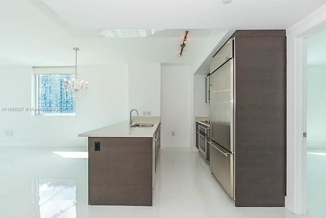 kitchen with an inviting chandelier, stainless steel built in fridge, sink, decorative light fixtures, and dark brown cabinetry