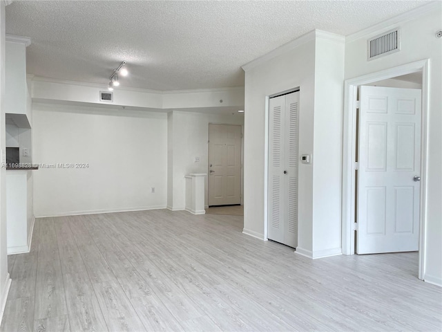 empty room with crown molding, light wood-type flooring, and a textured ceiling