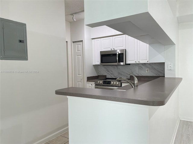 kitchen featuring electric panel, kitchen peninsula, decorative backsplash, appliances with stainless steel finishes, and white cabinetry