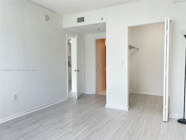 unfurnished bedroom with a walk in closet, a closet, a textured ceiling, and light wood-type flooring