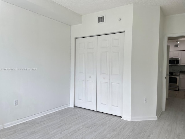 unfurnished bedroom with light wood-type flooring, a textured ceiling, and a closet