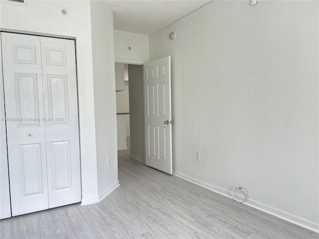 unfurnished bedroom with light hardwood / wood-style floors, a textured ceiling, and a closet