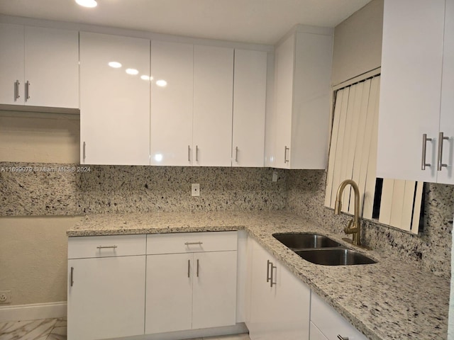 kitchen with tasteful backsplash, light stone countertops, sink, and white cabinets