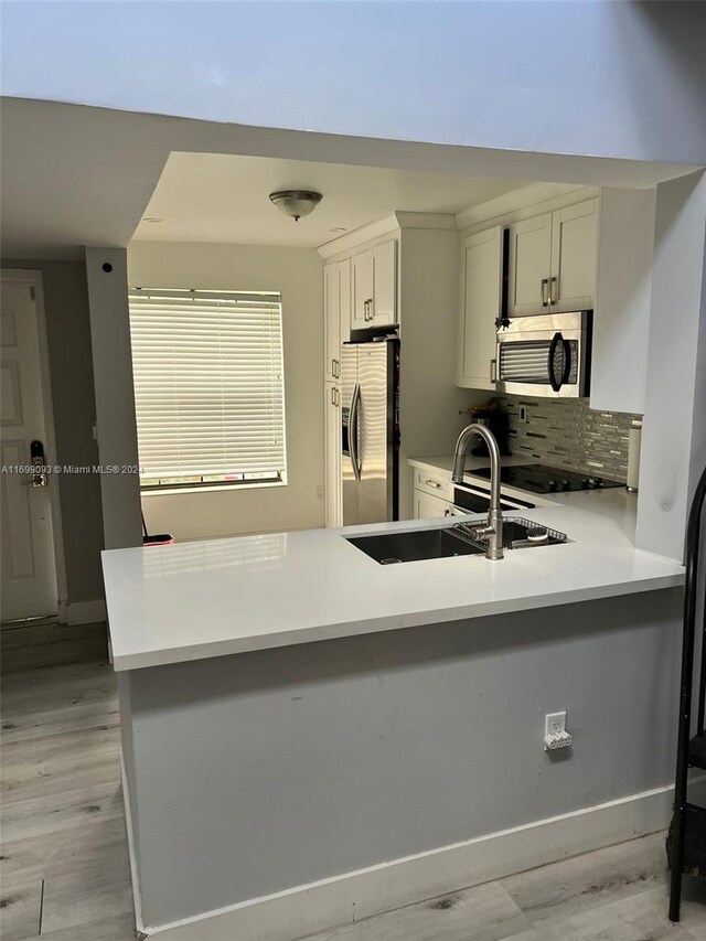 kitchen with decorative backsplash, light hardwood / wood-style floors, kitchen peninsula, and appliances with stainless steel finishes