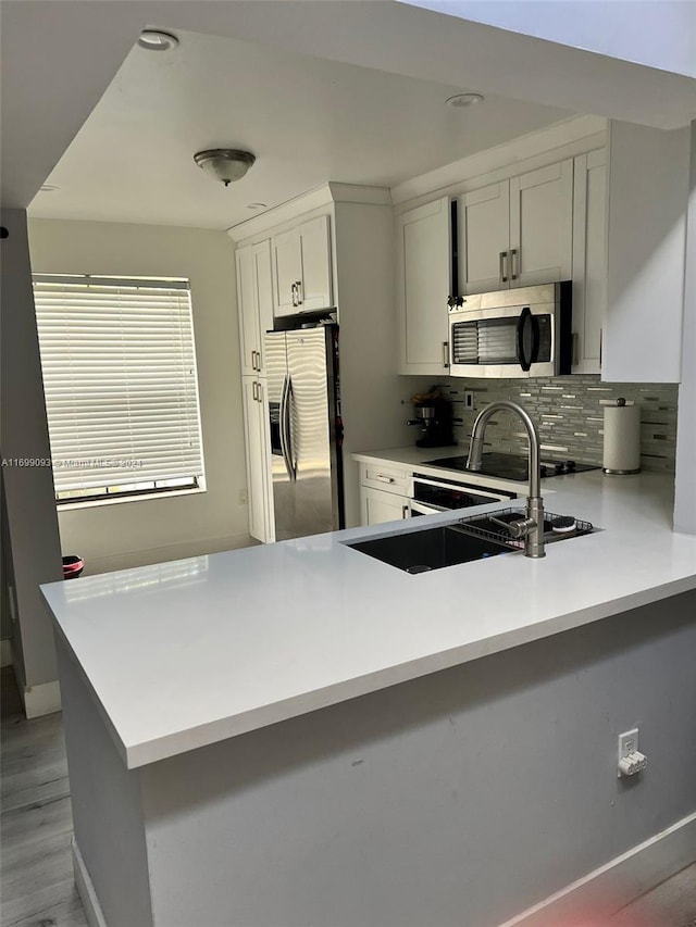 kitchen featuring white cabinetry, tasteful backsplash, light hardwood / wood-style floors, kitchen peninsula, and stainless steel appliances