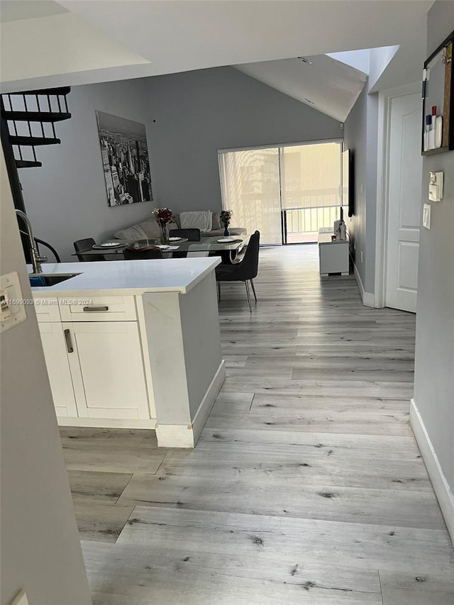 interior space featuring lofted ceiling, light hardwood / wood-style floors, white cabinetry, and sink