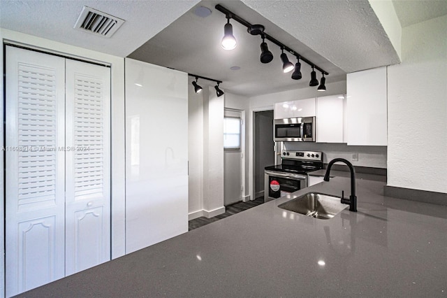 kitchen featuring track lighting, sink, a textured ceiling, white cabinetry, and stainless steel appliances