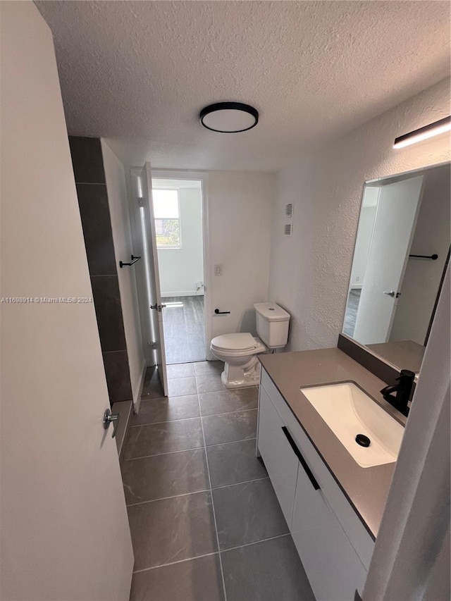 bathroom with tile patterned flooring, vanity, toilet, and a textured ceiling