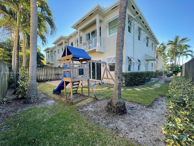 rear view of house with a playground, a yard, and a balcony