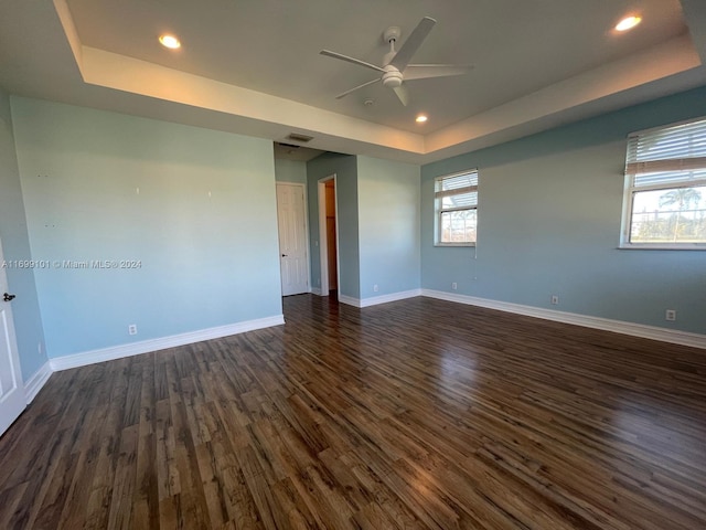 empty room featuring ceiling fan, dark hardwood / wood-style flooring, and a tray ceiling