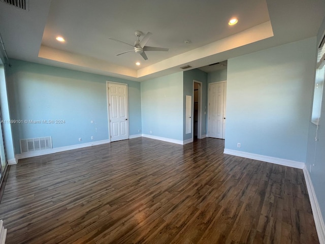 unfurnished room featuring a tray ceiling, dark hardwood / wood-style floors, and ceiling fan