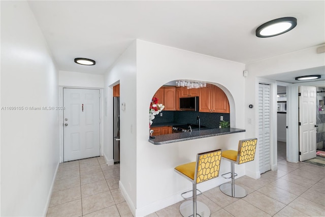 kitchen featuring backsplash, dark stone counters, light tile patterned floors, appliances with stainless steel finishes, and kitchen peninsula