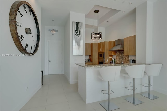 kitchen with pendant lighting, a breakfast bar, stainless steel microwave, wall chimney range hood, and kitchen peninsula