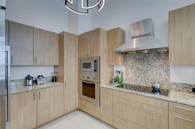 kitchen with light stone countertops, light brown cabinets, stainless steel appliances, and wall chimney range hood