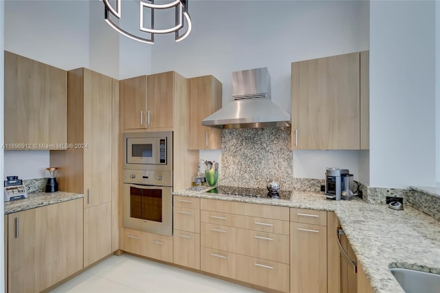 kitchen featuring appliances with stainless steel finishes, light brown cabinets, light stone counters, and wall chimney range hood