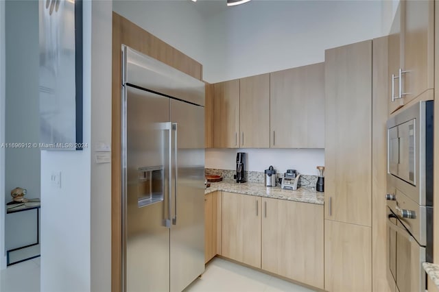 kitchen with built in appliances, light stone countertops, and light brown cabinets