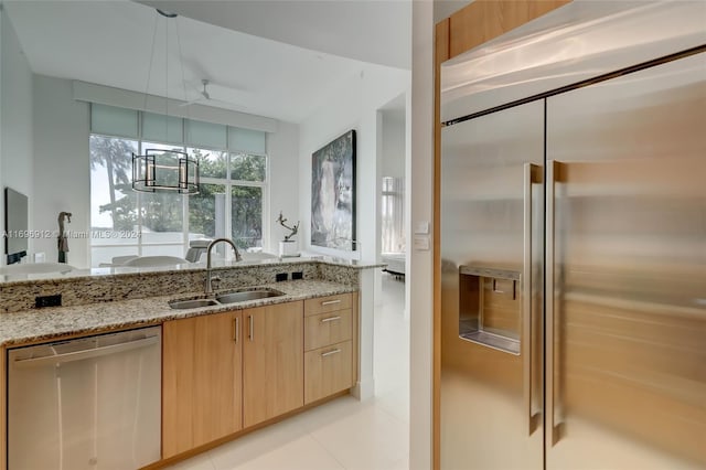 kitchen with light brown cabinets, sink, light tile patterned floors, light stone countertops, and appliances with stainless steel finishes