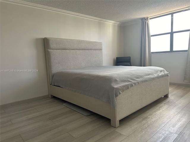 bedroom featuring light hardwood / wood-style flooring, a textured ceiling, and ornamental molding