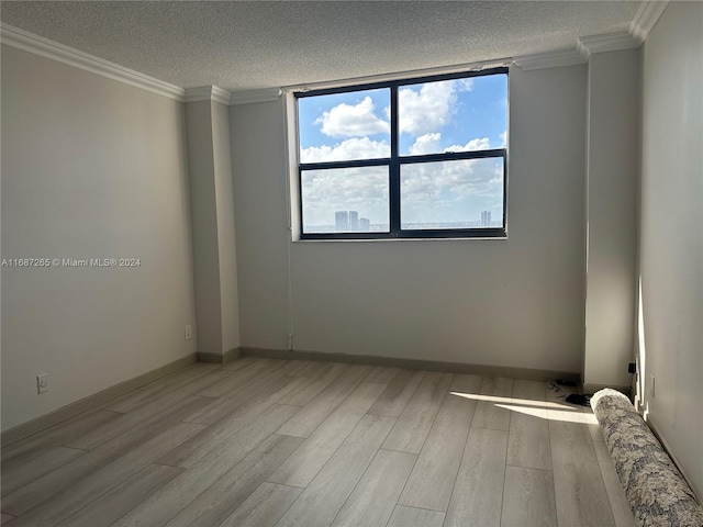 empty room with a textured ceiling, light wood-type flooring, and crown molding