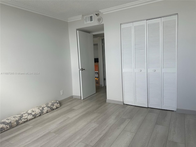 unfurnished bedroom featuring a closet, light hardwood / wood-style floors, a textured ceiling, and ornamental molding