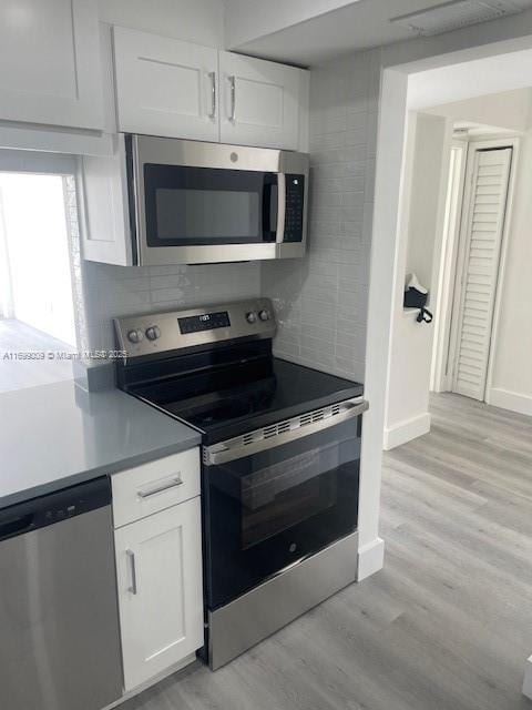 kitchen with stainless steel appliances, decorative backsplash, white cabinets, and light hardwood / wood-style flooring