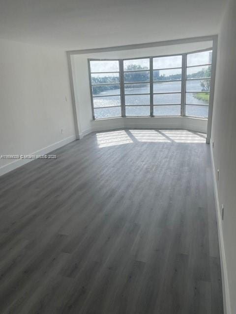 unfurnished room featuring a wealth of natural light, dark hardwood / wood-style floors, and a water view